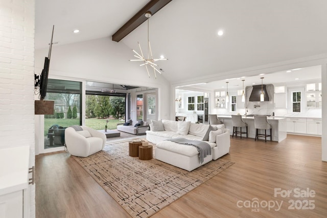 living room with a wealth of natural light, beamed ceiling, light wood-style flooring, and an inviting chandelier