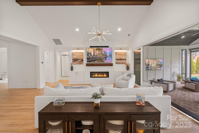 living room featuring a notable chandelier, a fireplace, visible vents, light wood-style flooring, and high vaulted ceiling