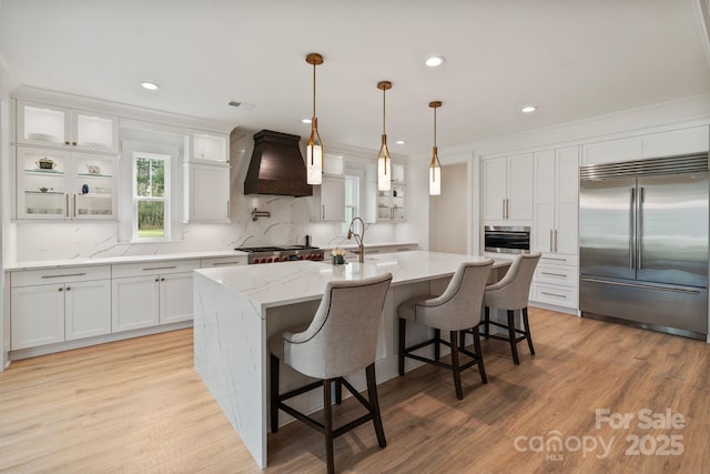 kitchen featuring stainless steel appliances, premium range hood, light wood-style flooring, and white cabinetry