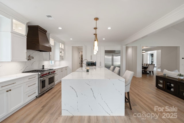 kitchen featuring light wood finished floors, visible vents, custom range hood, high quality appliances, and backsplash