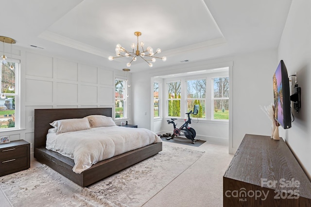 bedroom with a tray ceiling, multiple windows, carpet flooring, and a decorative wall