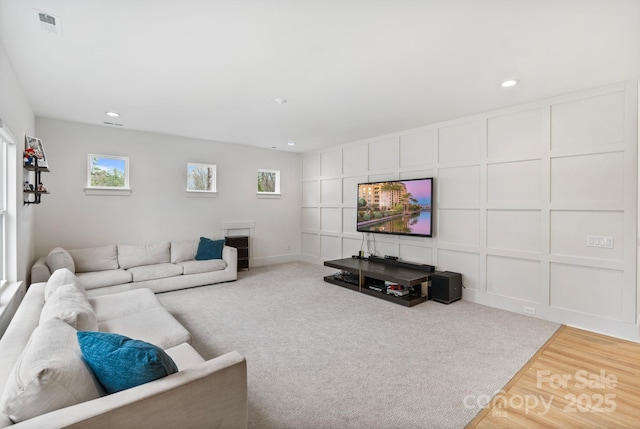 living area featuring recessed lighting, visible vents, a decorative wall, and wood finished floors