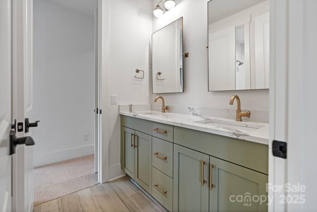 full bathroom featuring wood finished floors, a sink, baseboards, and double vanity