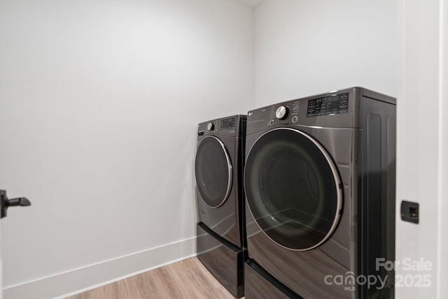 washroom featuring washing machine and dryer, laundry area, baseboards, and wood finished floors