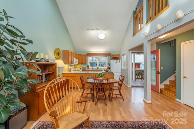 dining room with high vaulted ceiling, track lighting, baseboards, and light wood finished floors