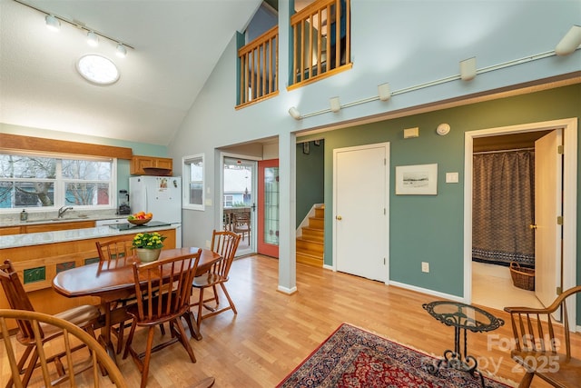 dining space featuring baseboards, stairway, rail lighting, light wood-style floors, and high vaulted ceiling