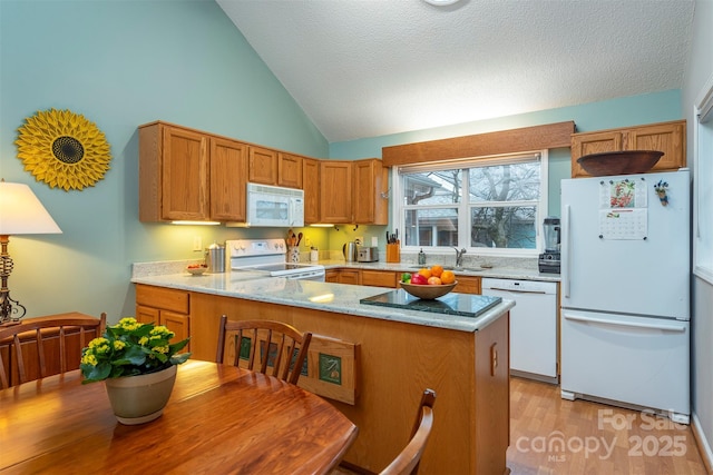 kitchen featuring white appliances, a peninsula, vaulted ceiling, light wood-style floors, and a sink