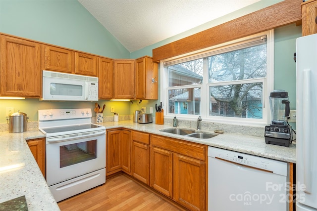 kitchen featuring white appliances, lofted ceiling, a textured ceiling, light wood-type flooring, and a sink