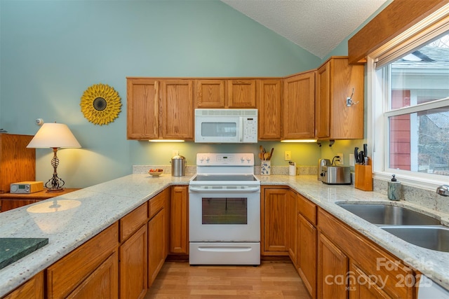 kitchen with white appliances, brown cabinets, vaulted ceiling, a textured ceiling, and a sink