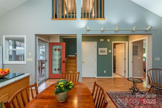 dining room with light wood finished floors, baseboards, stairs, and high vaulted ceiling