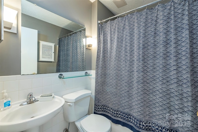 bathroom featuring tile walls, toilet, wainscoting, a sink, and a textured ceiling