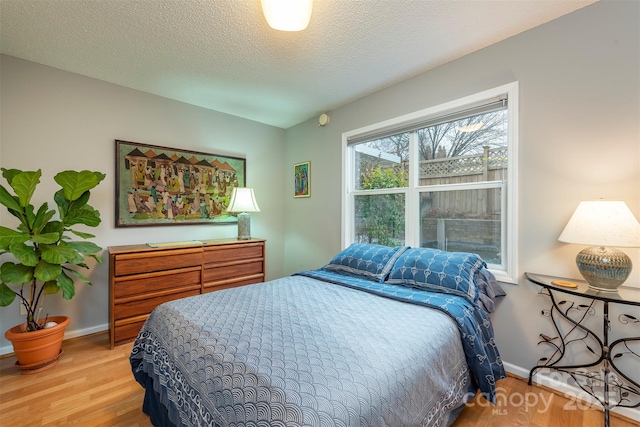 bedroom with a textured ceiling, baseboards, and wood finished floors