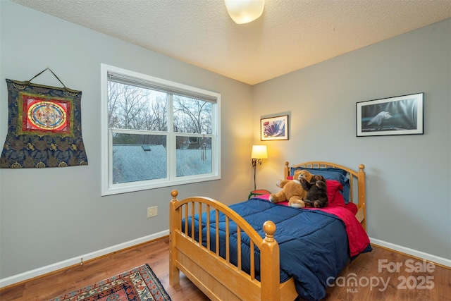 bedroom featuring a textured ceiling, baseboards, and wood finished floors