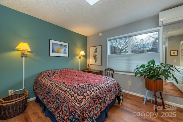 bedroom with a wall unit AC, a textured ceiling, baseboards, and wood finished floors