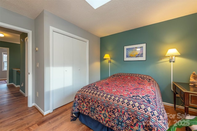 bedroom featuring a closet, a textured ceiling, baseboards, and wood finished floors