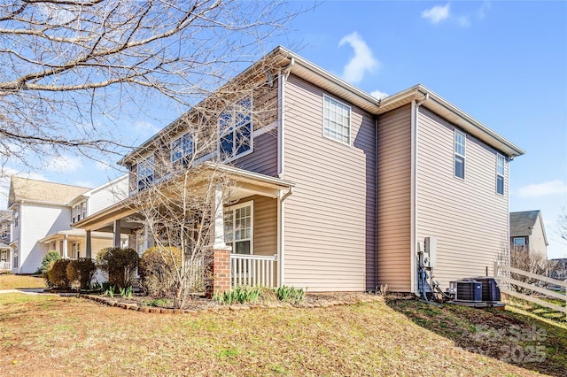 view of property exterior with cooling unit, a lawn, covered porch, and fence