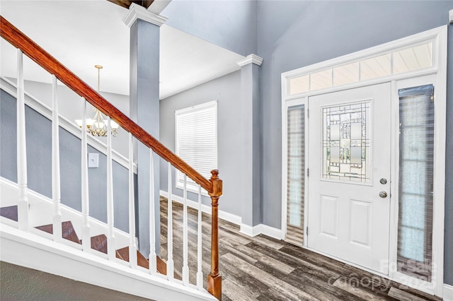 entryway featuring stairway, dark wood-type flooring, an inviting chandelier, and decorative columns