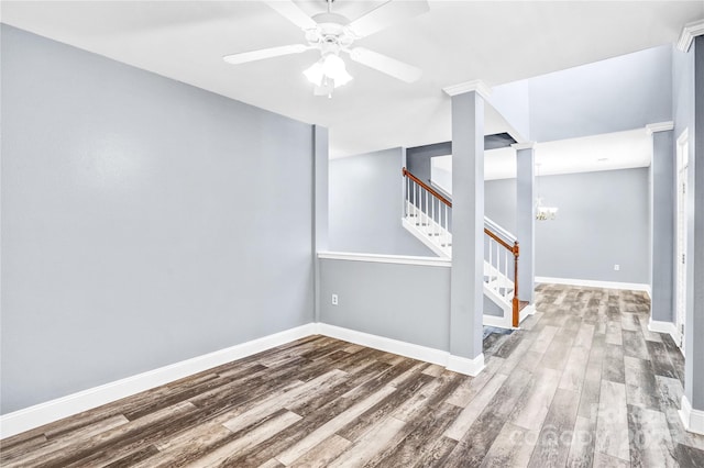 spare room featuring ceiling fan with notable chandelier, stairway, wood finished floors, and baseboards