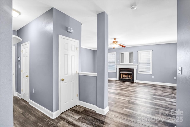 unfurnished living room featuring a fireplace with flush hearth, ceiling fan, dark wood-type flooring, and baseboards