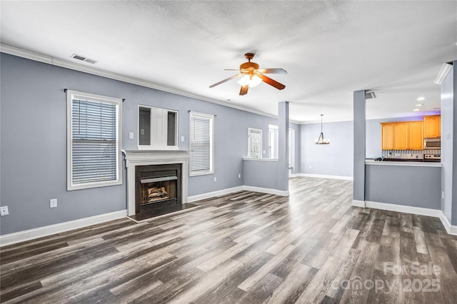 unfurnished living room featuring visible vents, ornamental molding, ceiling fan with notable chandelier, a fireplace, and dark wood-style flooring