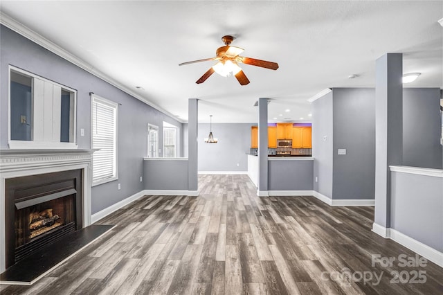 unfurnished living room with baseboards, a fireplace with raised hearth, ornamental molding, dark wood-type flooring, and ceiling fan with notable chandelier