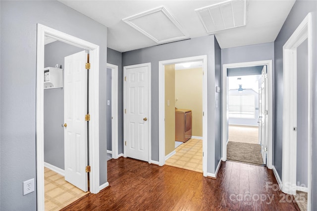 corridor with visible vents, baseboards, attic access, and wood finished floors