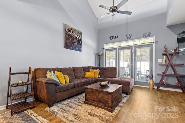 living area with hardwood / wood-style flooring, baseboards, high vaulted ceiling, and a ceiling fan