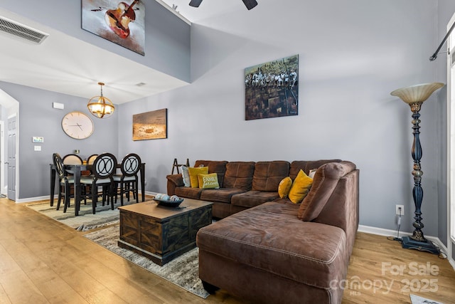 living room with baseboards, visible vents, wood finished floors, and ceiling fan with notable chandelier