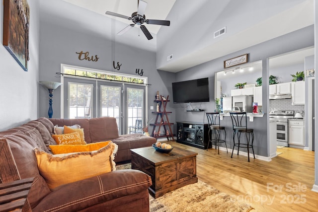 living room with a ceiling fan, visible vents, high vaulted ceiling, and light wood-style flooring