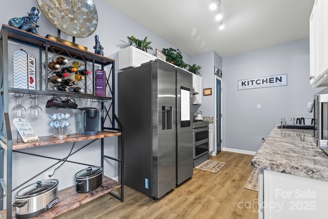 kitchen with baseboards, rail lighting, stainless steel appliances, light wood-style floors, and white cabinetry