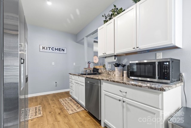 kitchen with white cabinets, dark stone countertops, stainless steel appliances, light wood-style floors, and a sink