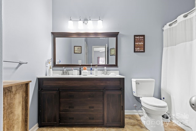 bathroom with baseboards, a sink, toilet, and double vanity