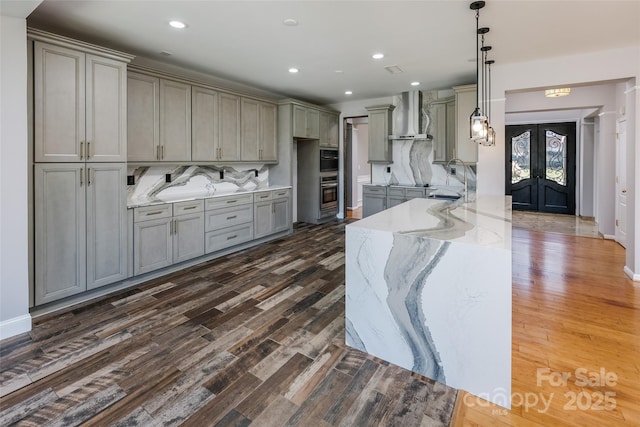 kitchen featuring gray cabinets, wall chimney range hood, french doors, and light stone countertops