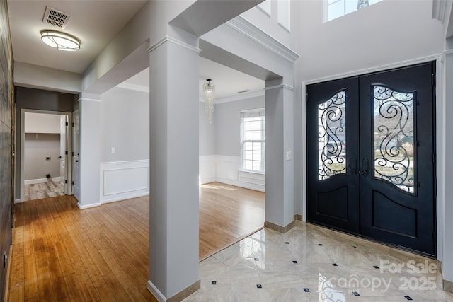 entryway with visible vents, a wainscoted wall, crown molding, french doors, and a decorative wall