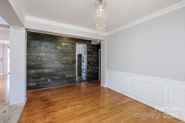 interior space with an inviting chandelier, an accent wall, crown molding, and wood finished floors