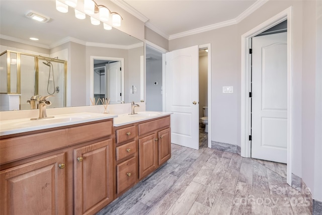 full bath with crown molding, double vanity, a stall shower, a sink, and wood finished floors