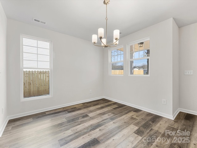 unfurnished room with an inviting chandelier, visible vents, baseboards, and wood finished floors