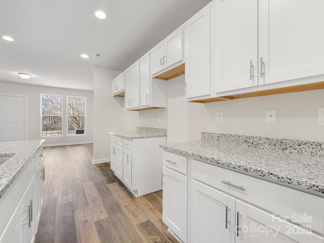 kitchen with light wood finished floors, baseboards, white cabinets, light stone countertops, and recessed lighting