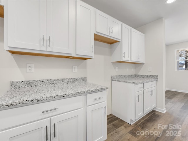 kitchen featuring white cabinetry, light stone counters, dark wood finished floors, and baseboards