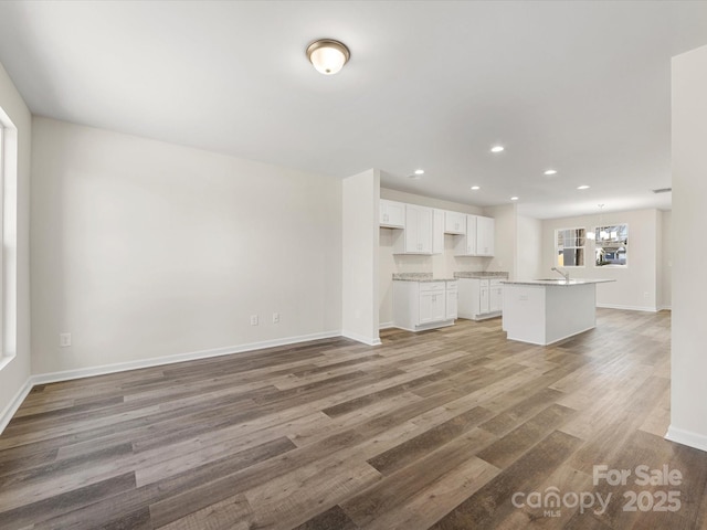 unfurnished living room featuring baseboards, light wood-style flooring, a chandelier, a sink, and recessed lighting