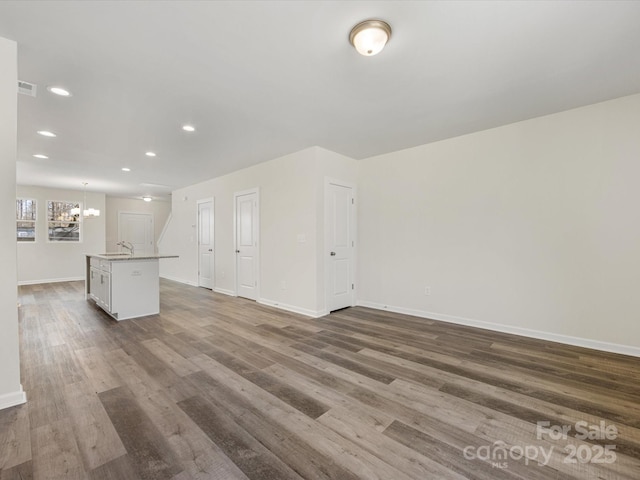 unfurnished living room with a chandelier, recessed lighting, baseboards, and wood finished floors