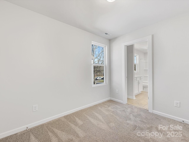 spare room featuring light colored carpet, visible vents, and baseboards