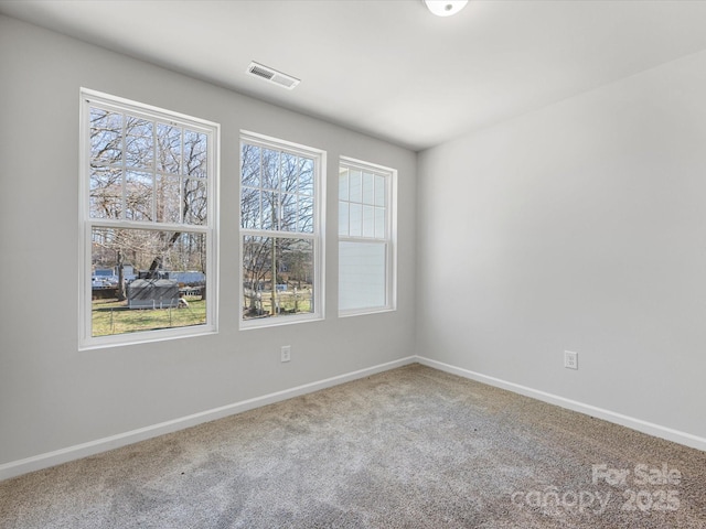 carpeted empty room featuring plenty of natural light, visible vents, and baseboards