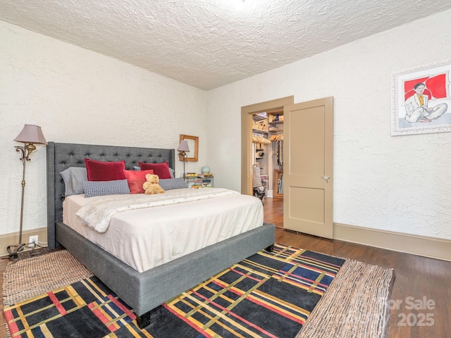 bedroom featuring a textured wall, a spacious closet, a textured ceiling, wood finished floors, and baseboards