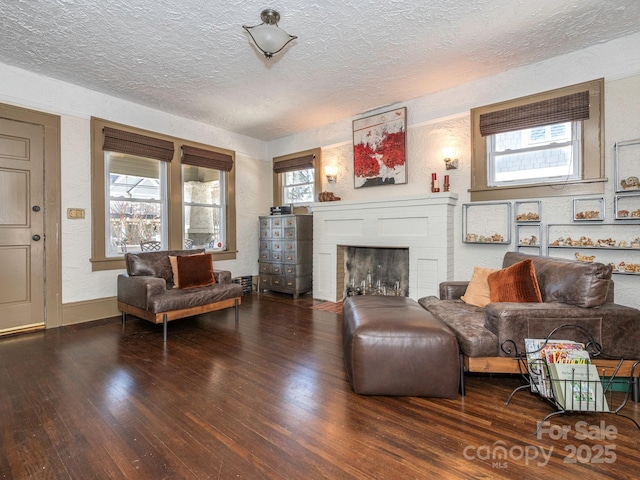 living room featuring a textured ceiling, a textured wall, baseboards, a brick fireplace, and wood-type flooring