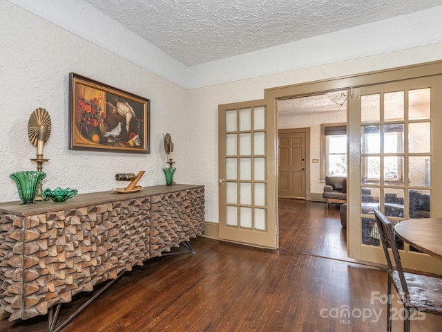 interior space featuring a textured ceiling, a textured wall, french doors, and hardwood / wood-style floors