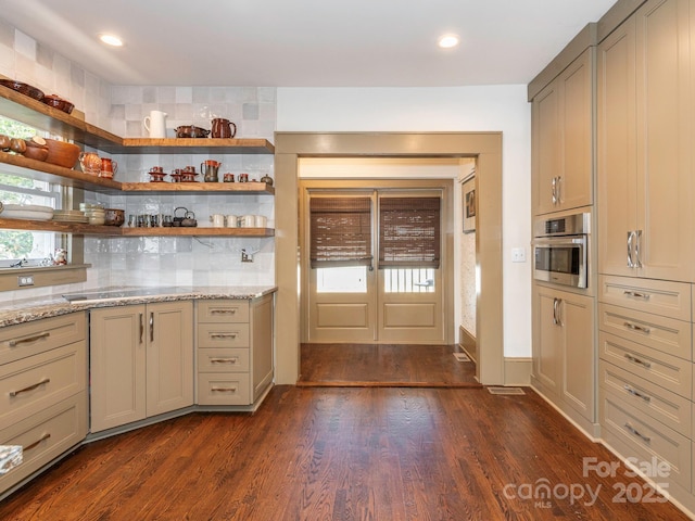 kitchen with dark wood-style floors, light stone countertops, stainless steel oven, backsplash, and recessed lighting