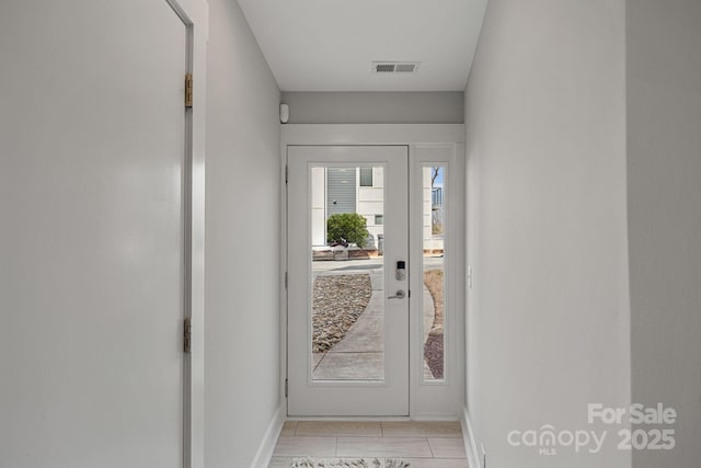 doorway to outside with baseboards, visible vents, and light tile patterned flooring