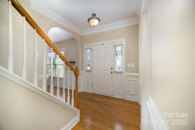 entryway with a decorative wall, a wainscoted wall, wood finished floors, stairs, and crown molding