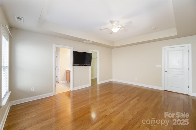 unfurnished living room with a tray ceiling, visible vents, and light wood-style floors